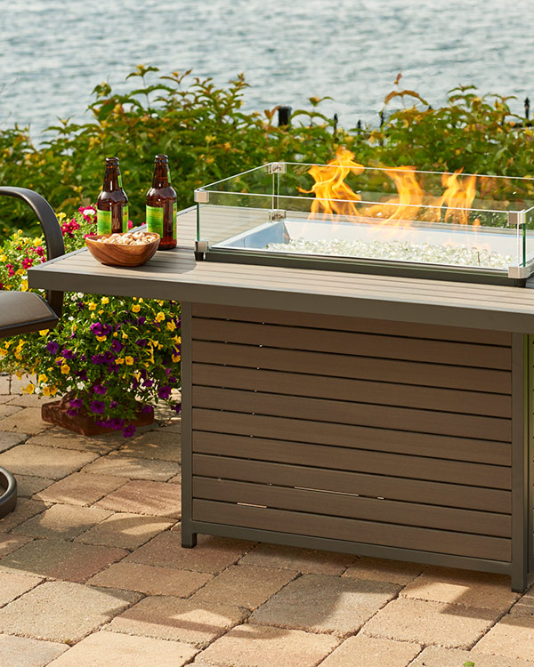 Brooks Fire Pit Table by the outdoor greatroom company in a lifestyle setting near water